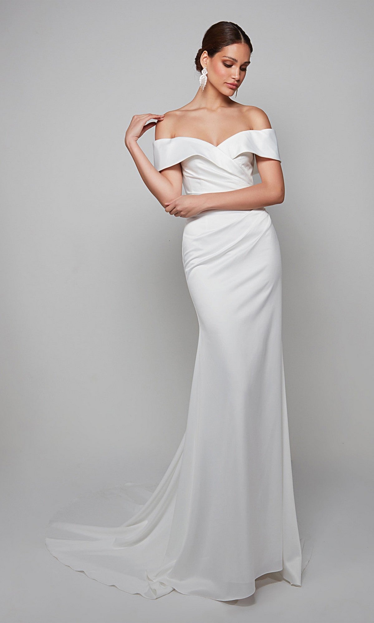 A woman models the Long White Dress: Alyce 7059, a floor-length white satin gown featuring an off-shoulder design, fitted bodice, and slight train, posed against a plain light gray background.